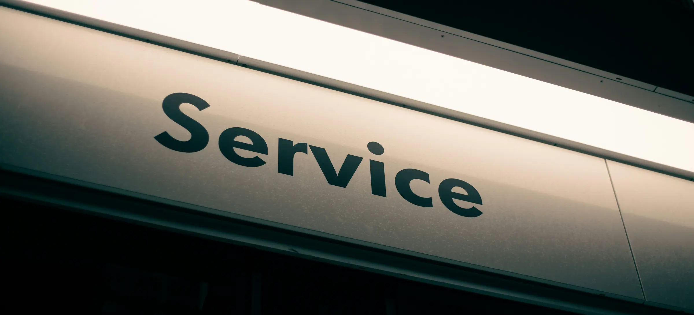 An illuminated shopfront sign reading Service, photographed from below against a dark facade